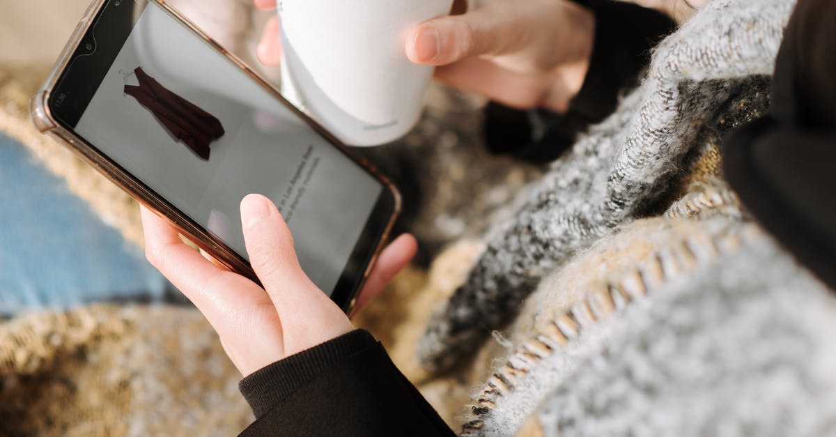 Duty-free shopping after 48 hours from US to Canada - From above of crop anonymous female purchaser with takeaway hot drink choosing dress on cellphone screen during online shopping