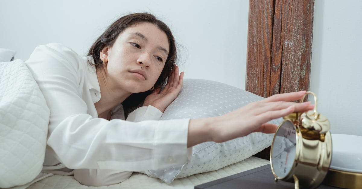 early morning rental car drop-off - sacramento international airport - Sleepy young brunette female in white sleepwear resting in comfortable bed and waking up with alarm clock at home in morning time