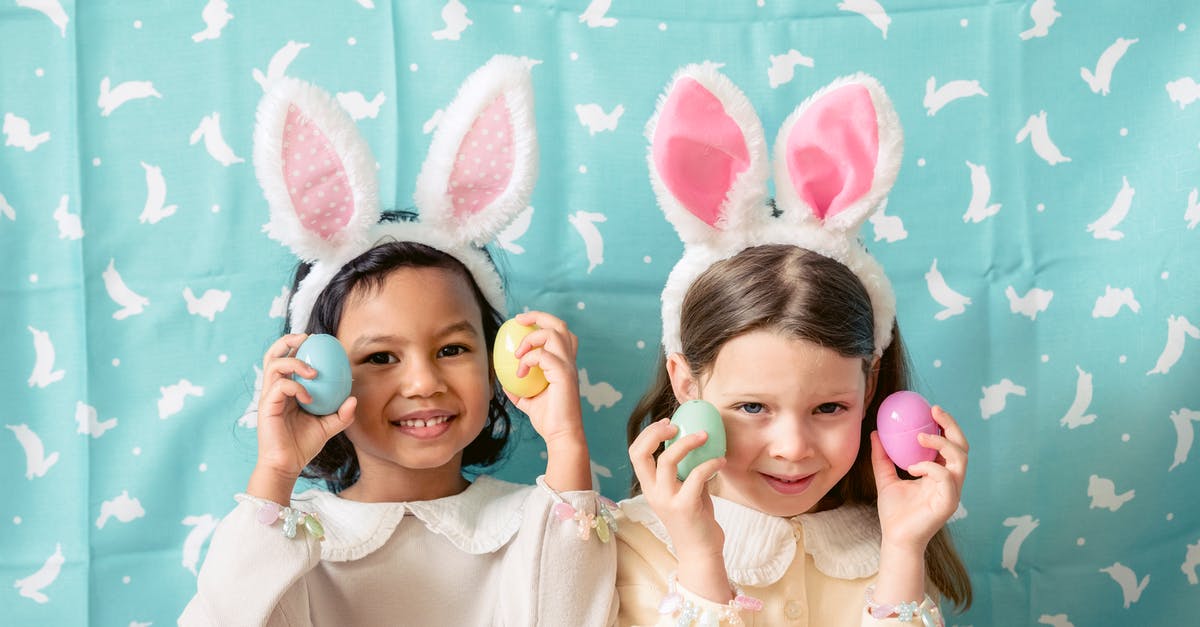 Easter egg in cabin baggage on Ryanair - Content diverse children in hairbands with bunny ears showing decorative eggs while looking at camera against fabric with rabbit ornament