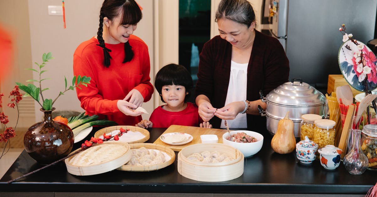 Eating pasta with raw minced meat in Italy - Cheerful Asian grandma with boy and female teen preparing dumplings at table with minced beef filling at home