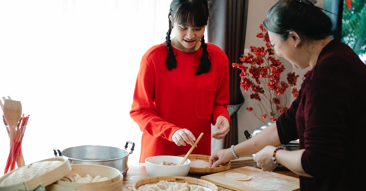 Eating pasta with raw minced meat in Italy - Smiling ethnic grandma with female teen preparing Chinese dumplings while talking at table with traditional steamers in house