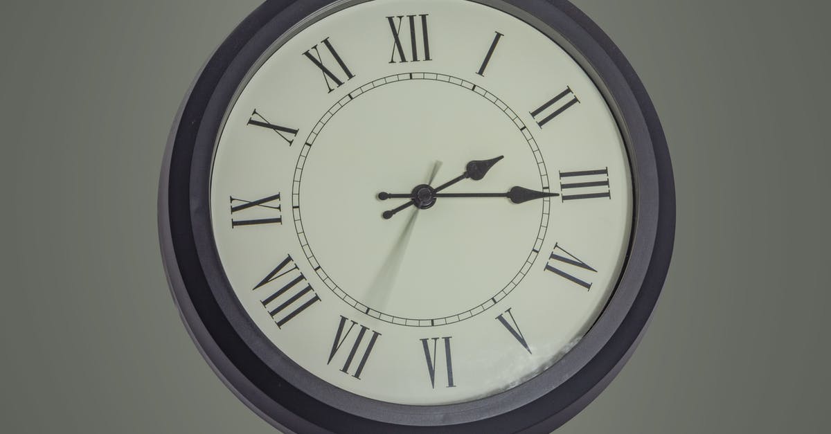 EC261 compensation for a delay between 3 and 4 hours - Round black mechanical clock with Roman numerals hanging on gray wall