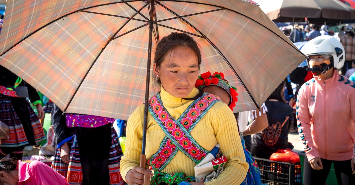 EC 261 refund: marketing vs operating carrier - Pensive ethnic mother with umbrella carrying unrecognizable toddler girl against crop people while looking down in bazaar