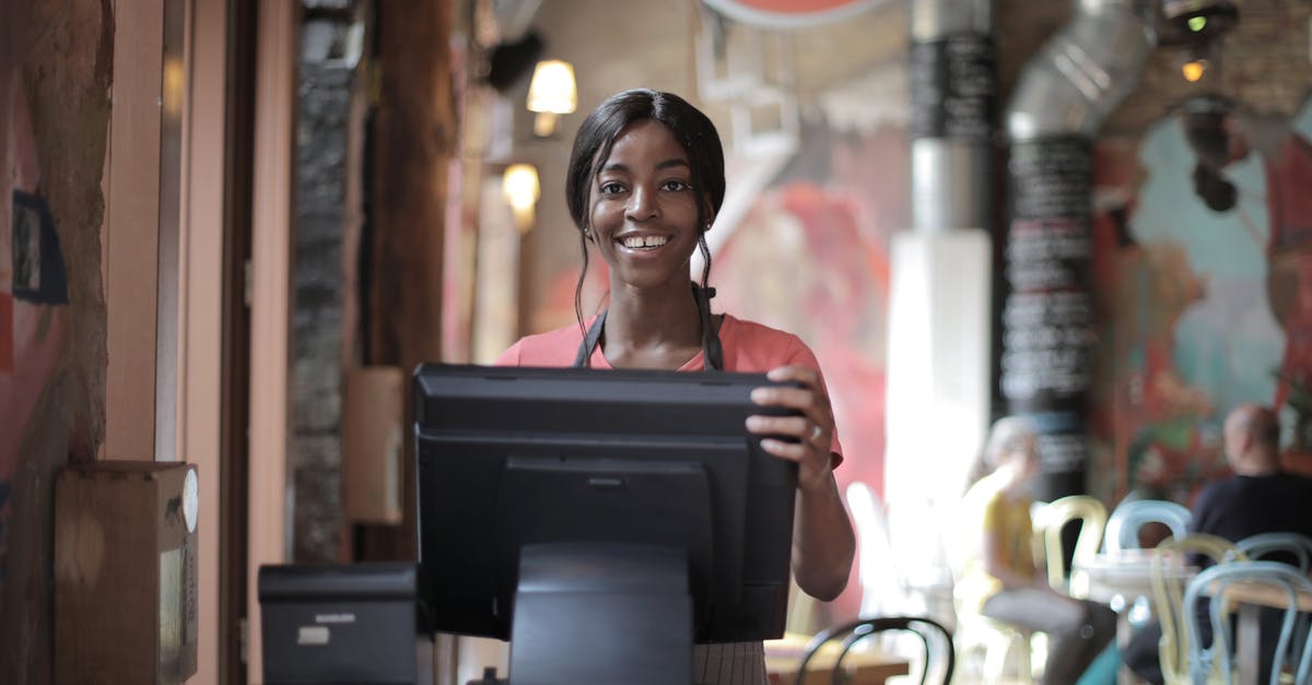 Economy ticket, but enjoy first-class service? - Positive young woman in uniform smiling while standing at counter desk in  cafe