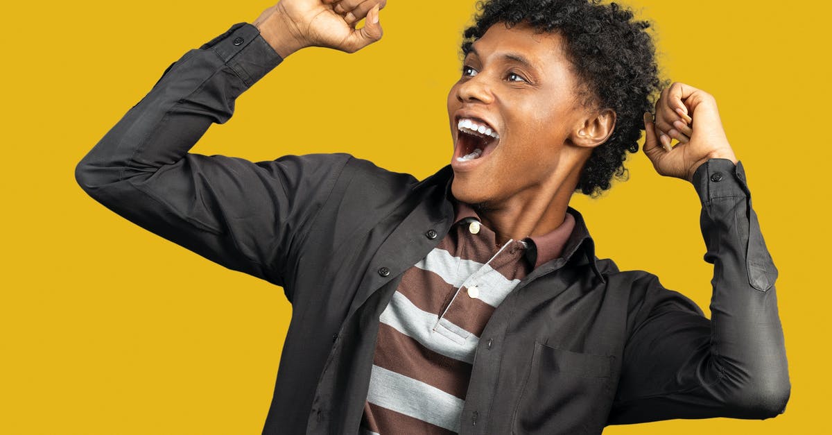 Effect of 10-year UK ban on US Visa Lottery winner - Expressive African American male wearing casual clothes standing against yellow background in studio and raising fists in triumph while looking away and screaming happily