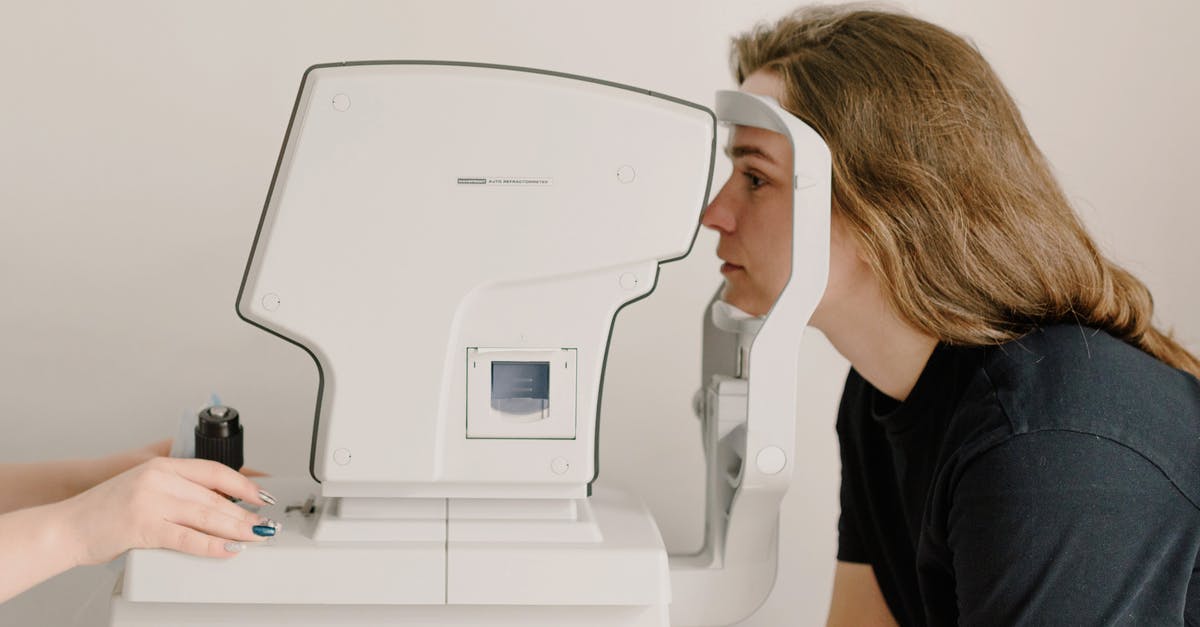 Electronic medical devices through British airport security - Side view of crop anonymous doctor checking eyesight of female patient using vision screening device in clinic