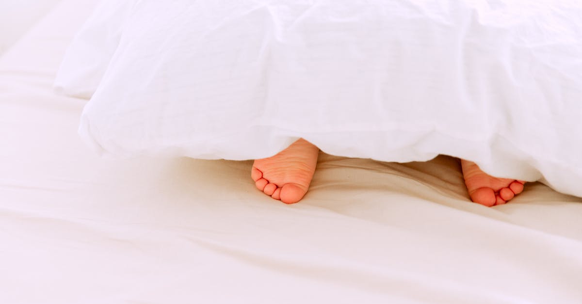 Eligibility for a compensation under EC/261 - Crop tiny feet of little child lying under white blanket on comfortable bed in light bedroom at home