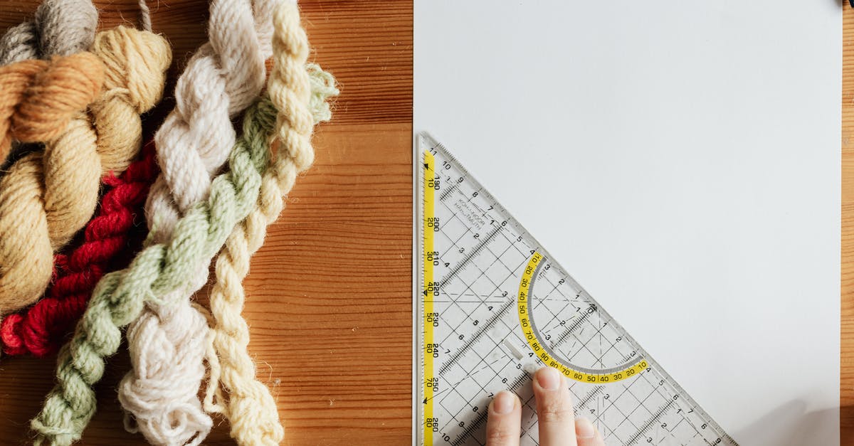 Emirates Business Class Overhead Bin - Top view of unrecognizable female weaver preparing template for future carpet on piece of paper using triangular protractor sitting at wooden table with yarn twists