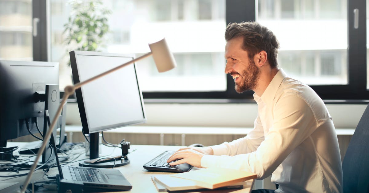 Emirates contact via email - Man in White Dress Shirt Sitting on Black Rolling Chair While Facing Black Computer Set and Smiling