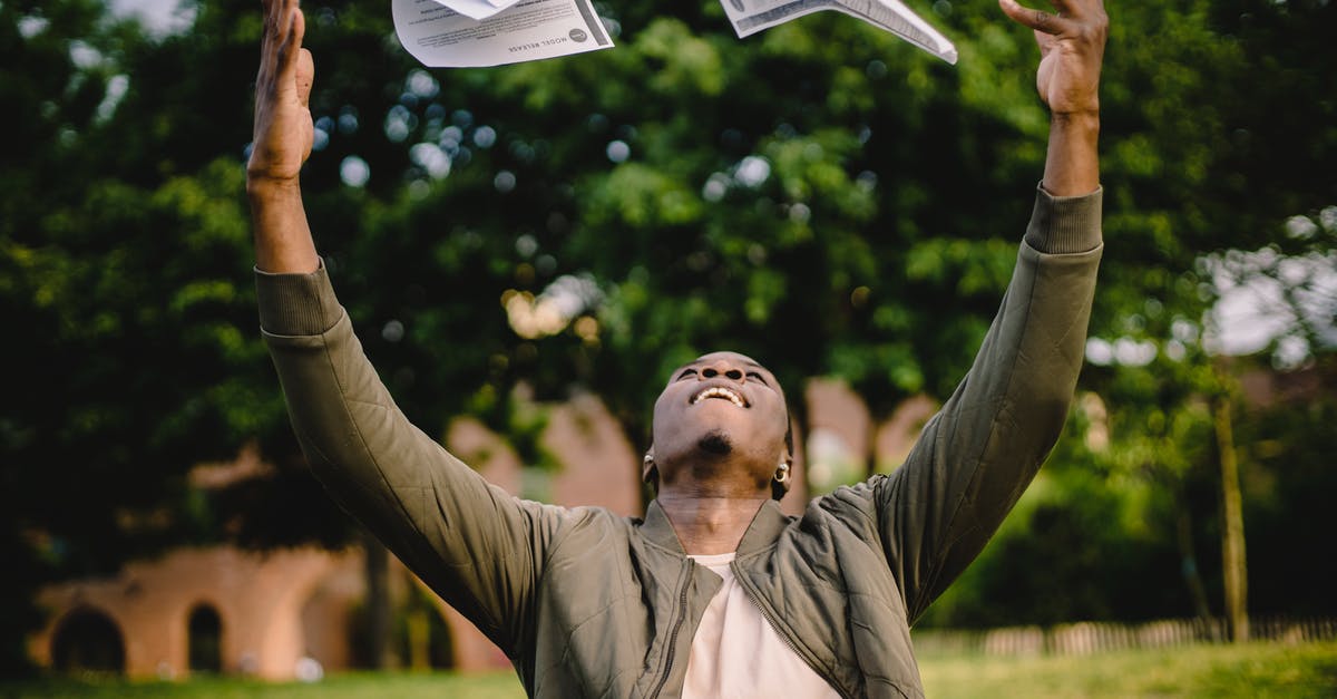 Entering air ticket costs in a UK Visa application - Happy African American remote worker tossing papers in air happy to get rid of boring paperwork while sitting in green park