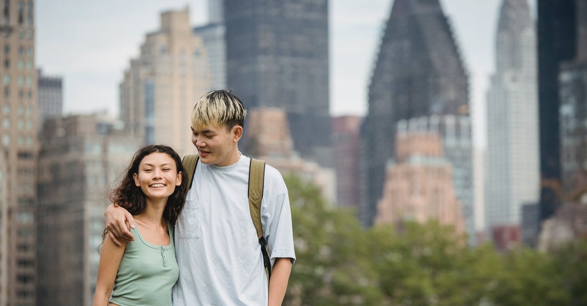 Entering US a few days before B1/B2 visa expiration date - Cheerful young Asian couple in casual clothes hugging each other and standing against modern skyscrapers while spending holidays in New York