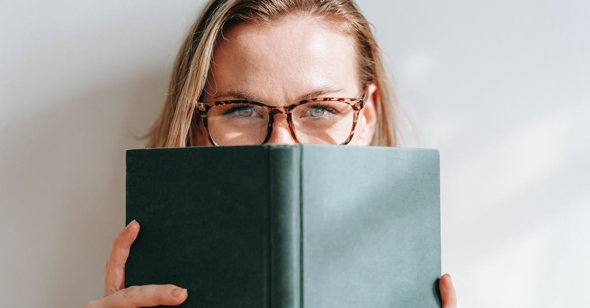 Entry as tourist with intent to stay as student [closed] - Clever young blond female in eyeglasses covering face with book while looking at camera on light background