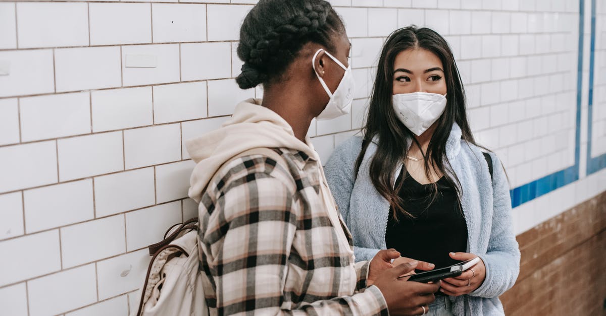 Entry into Canada for Candian citizens during COVID-19 period [duplicate] - Unrecognizable black woman with rucksack talking to Asian girlfriend in respiratory mask with cellphone near tiled brick wall during coronavirus period