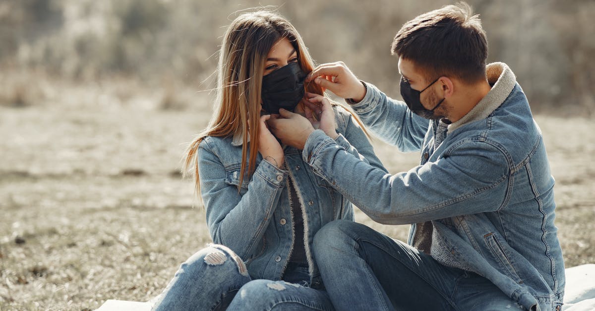 ESTA 90 day start date - Cheerful young couple in black medical masks resting on plaid on sunny meadow in countryside