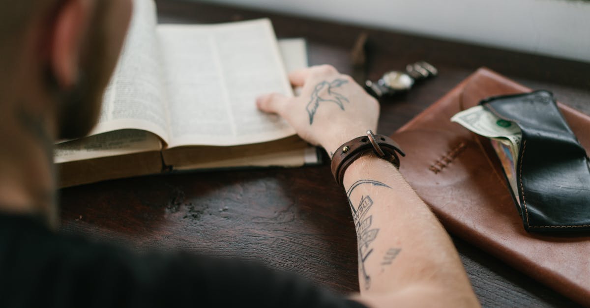 E-Ticket vs Itinerary vs Booking Reference - Back view of crop tattoed male student wearing elegant watch reading old books in library at desk with leather wallet and envelope