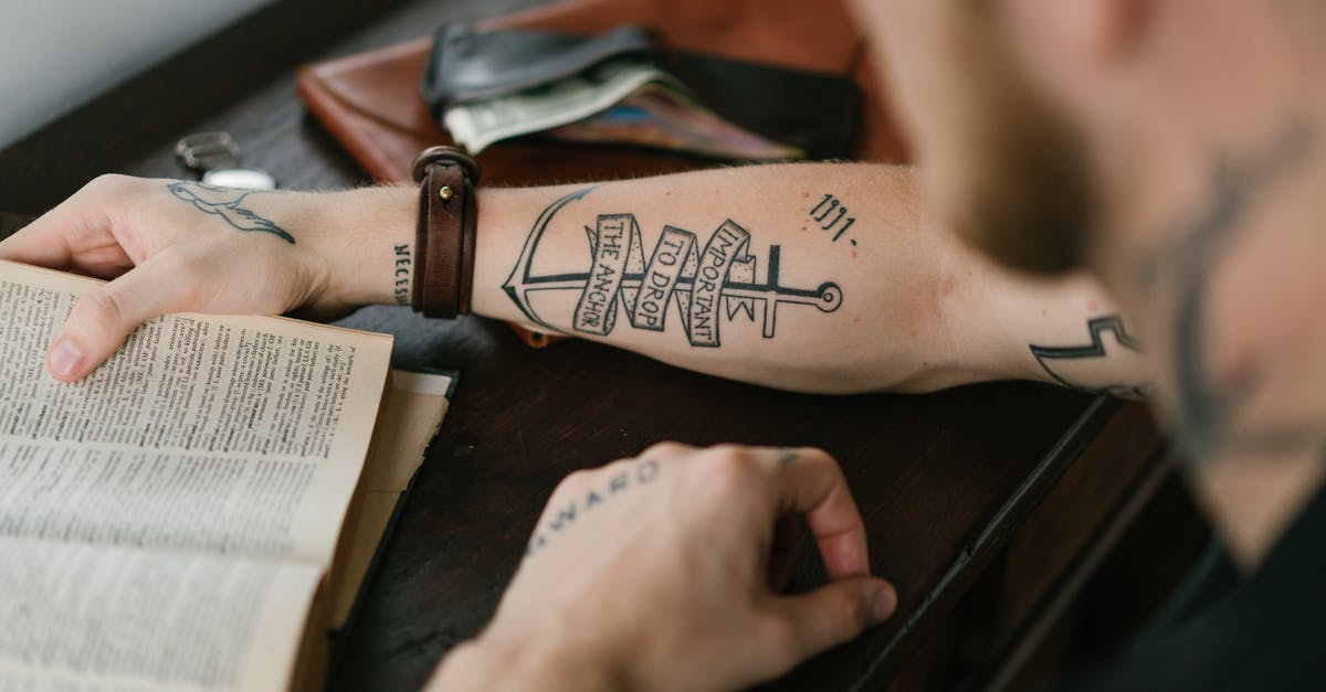 E-Ticket vs Itinerary vs Booking Reference - Crop man with tattoo on arm reading old book