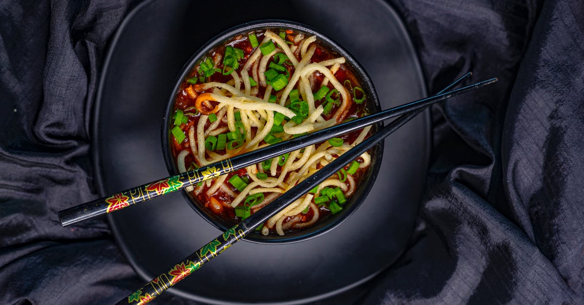 Etiquette of eating noodle soup in China - Top view of black bowl with Asian soup with noodle and green onion served with bamboo chopsticks on black tablecloth