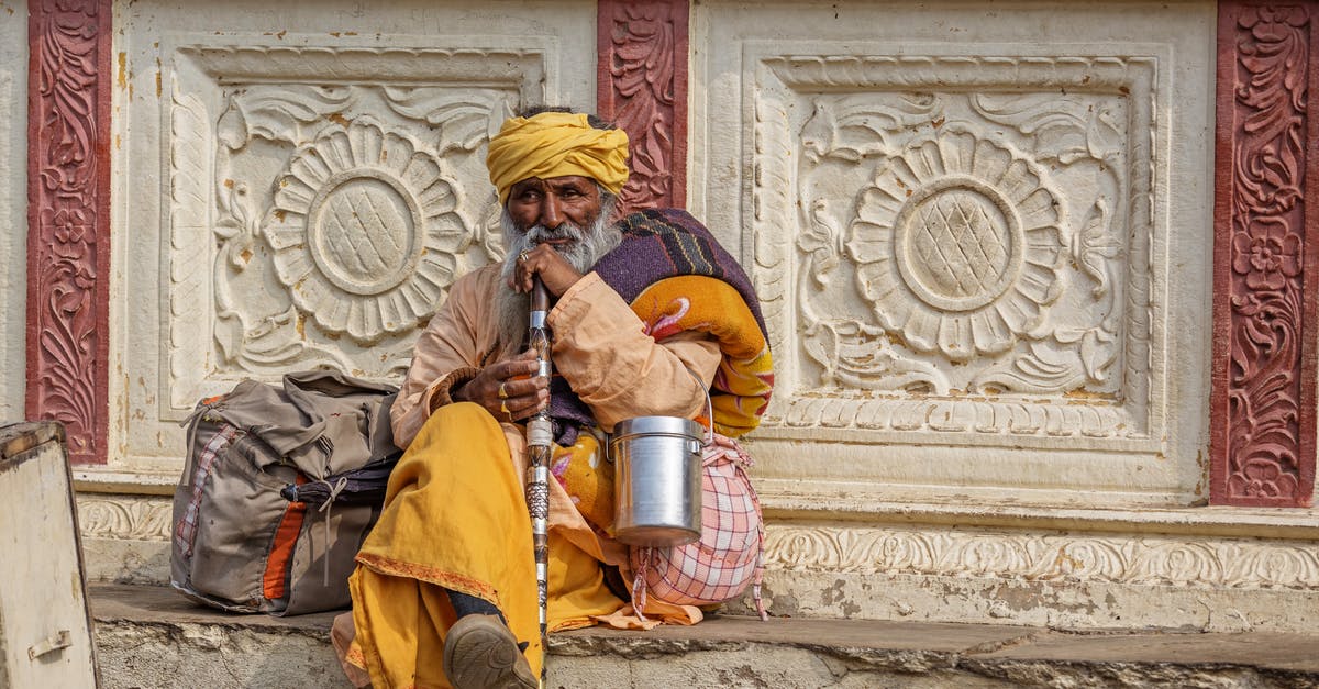 Etiquette when staying with an indigenous community - Full body of elderly Indian man in colorful turban sitting with belongings and ornamental cane on street