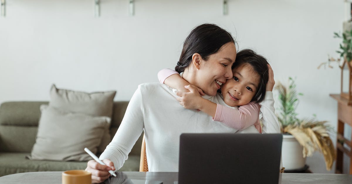 EU261, cancelled connection and predating duty of care - Happy young Asian woman working remotely from home with laptop and tablet while adorable little daughter hugging from behind