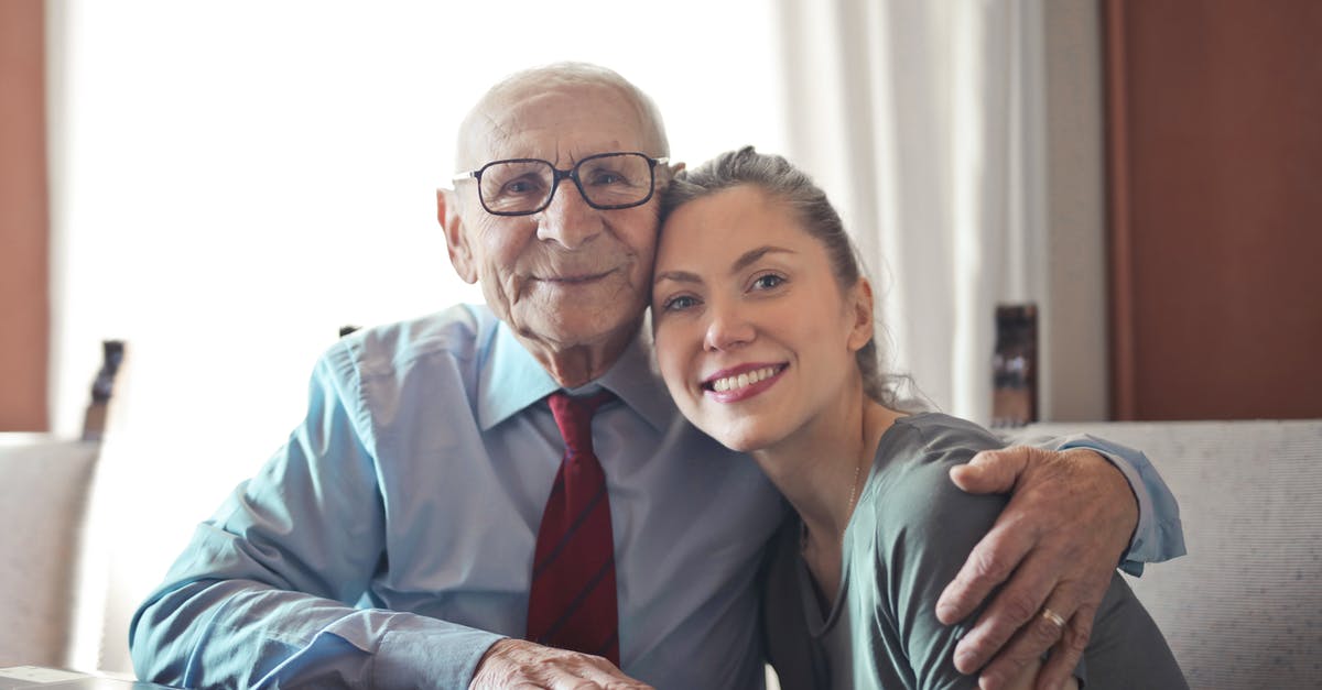 EU261, cancelled connection and predating duty of care - Positive senior man in formal wear and eyeglasses hugging with young lady while sitting at table