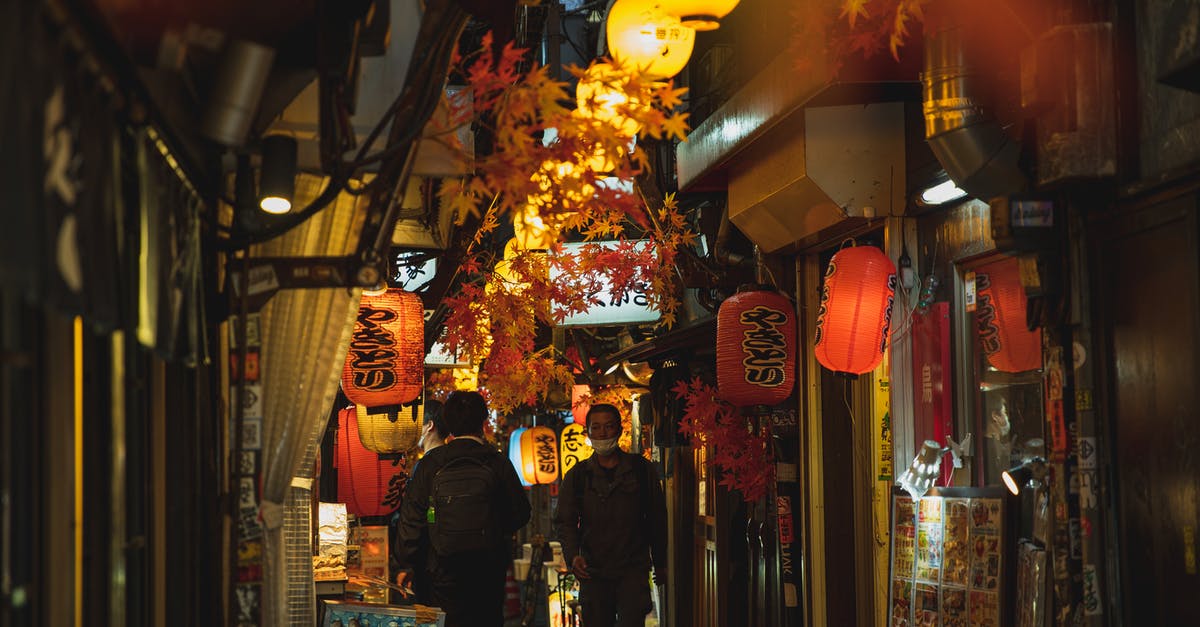 EU DCC/covid restrictions and layovers - Men in protective face masks walking along narrow empty bright street in Asian sity