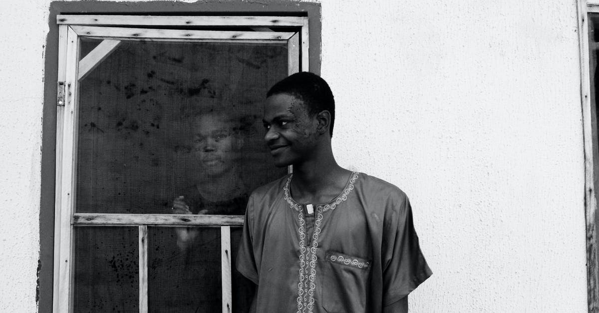 EU roaming when calling a number outside the EU? - Black and white of slim happy African American guy looking away while standing near house with concrete walls and old window with serious partner inside building