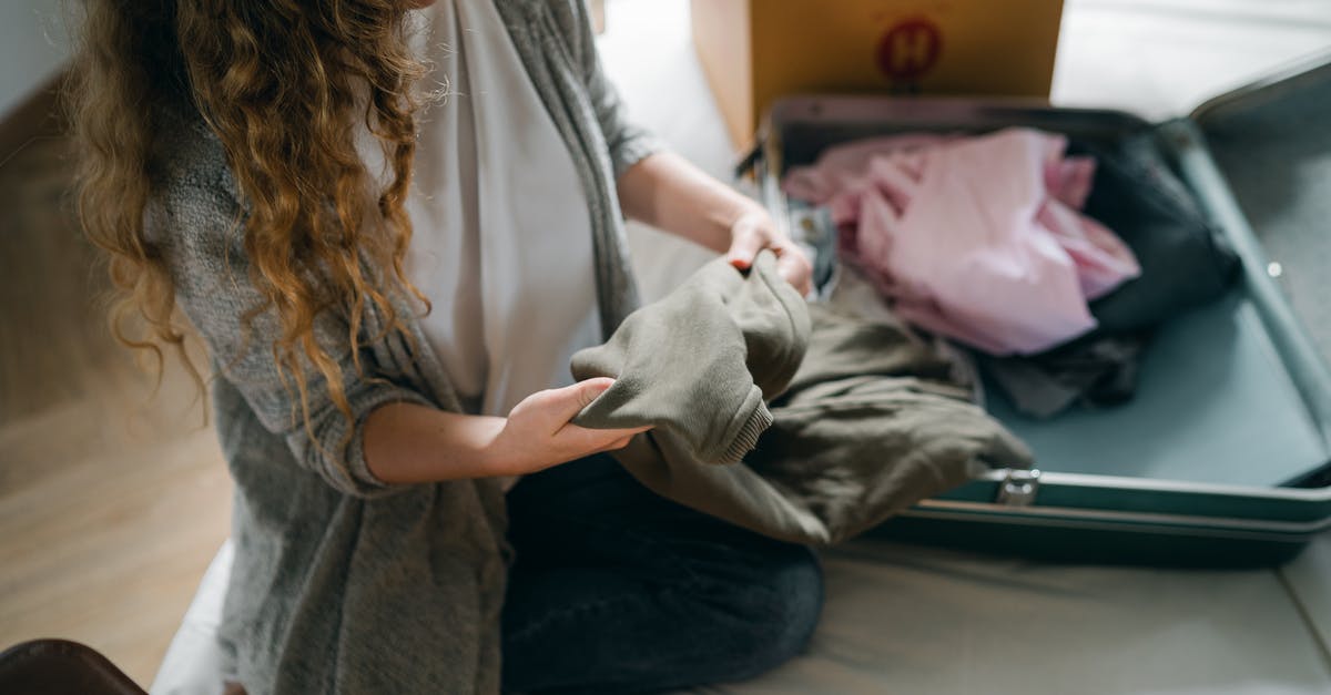 Excess baggage to Kenya from Geneva - From above crop anonymous female in casual wear sitting on bed and packing luggage while preparing to move out