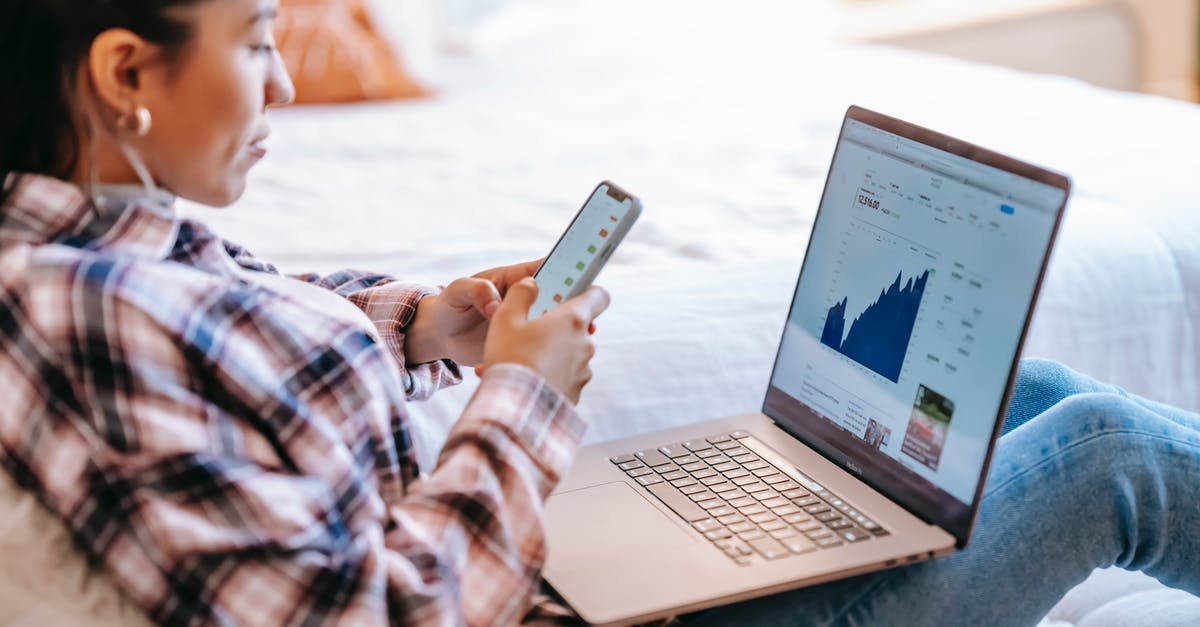 Exchanging and using Scottish pounds - Side view of crop ethnic female dealer using trading app on cellphone against netbook with graph on screen in house