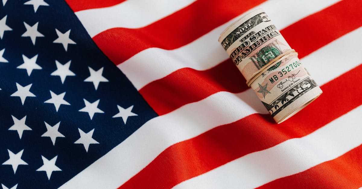 Exchanging money at bank vs at airport - From above of United States currency folded in roll placed on USA flag illustrating concept of business profit and wealth