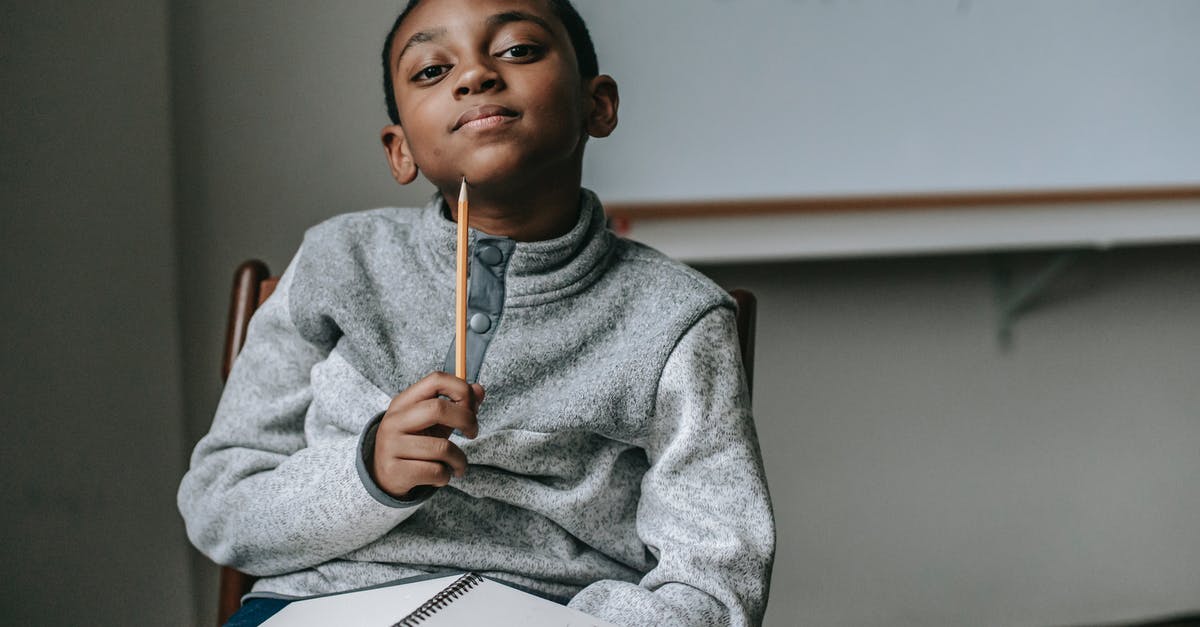 Excursion inside British Rail Class 55 "Deltic" - Cute little black boy wearing fleece sweater sitting on chair with pencil under chin and dreamy looking at camera during break after lesson in school