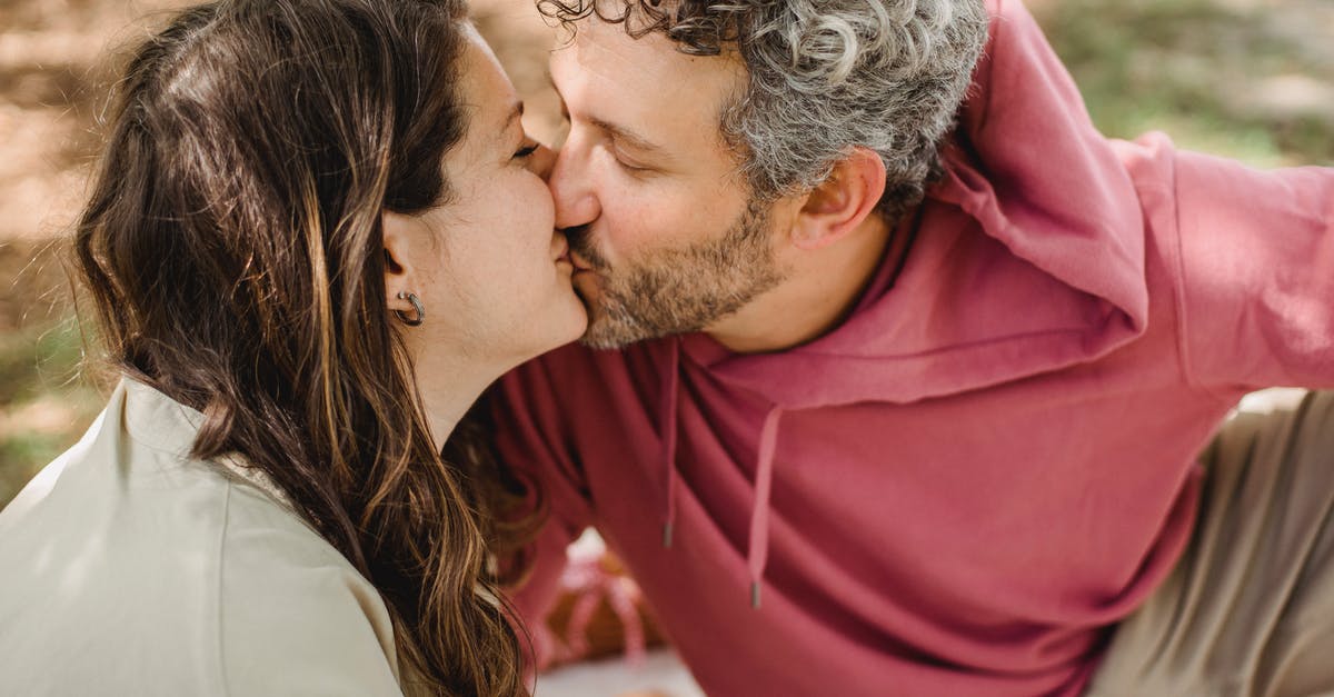 Expected arrival date changed - Australian Visitor 600 Visa - Side view of romantic wife and husband kissing each other while sitting on blanket on blurred background during picnic in nature