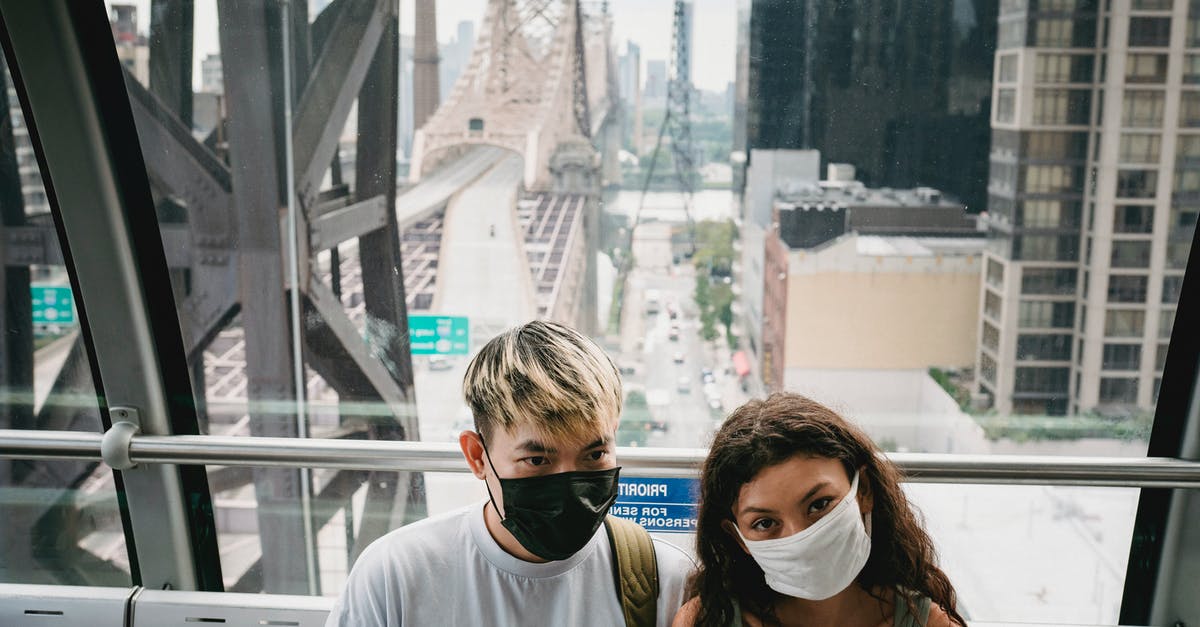 Experience of US CBP as solo traveler [closed] - Young couple in casual outfit and protective face masks riding cableway cabin along urban New York City district near Queensboro Bridge during coronavirus outbreak