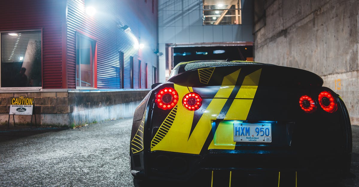 Expired license and registration while car traveling within the US - Rear bumper of modern car with ornament on asphalt roadway between buildings illuminated by shiny lamps at dusk