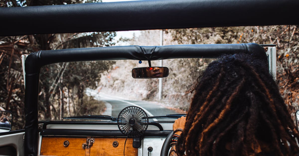 Explore Alps without a car - Back view of unrecognizable traveler with stylish dreadlocks spinning steering wheel while driving car and reflecting in small mirror