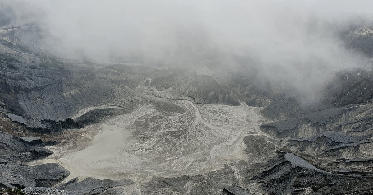 Exporting Lava Stones from Tenerife within EU - From above severe view of rough volcanic crater with hot foamy water and rocky peaks covered with dense mysterious haze