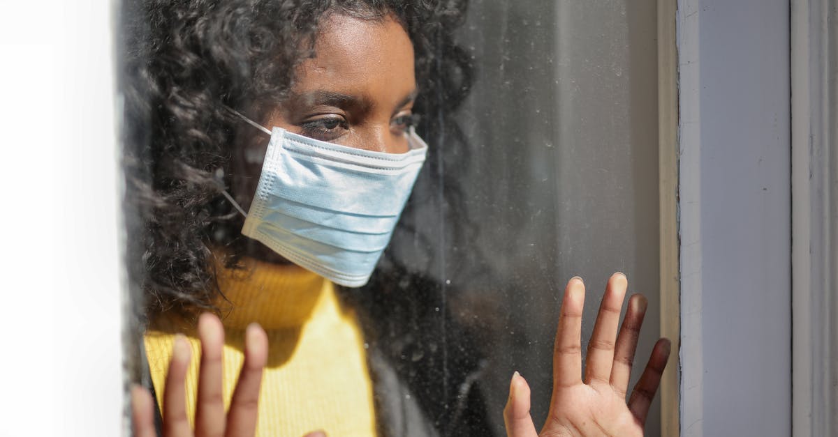 Extension of stay at USA due to COVID-19 lockdown - Serious young ethnic lady in medical mask standing near window and looking away on street