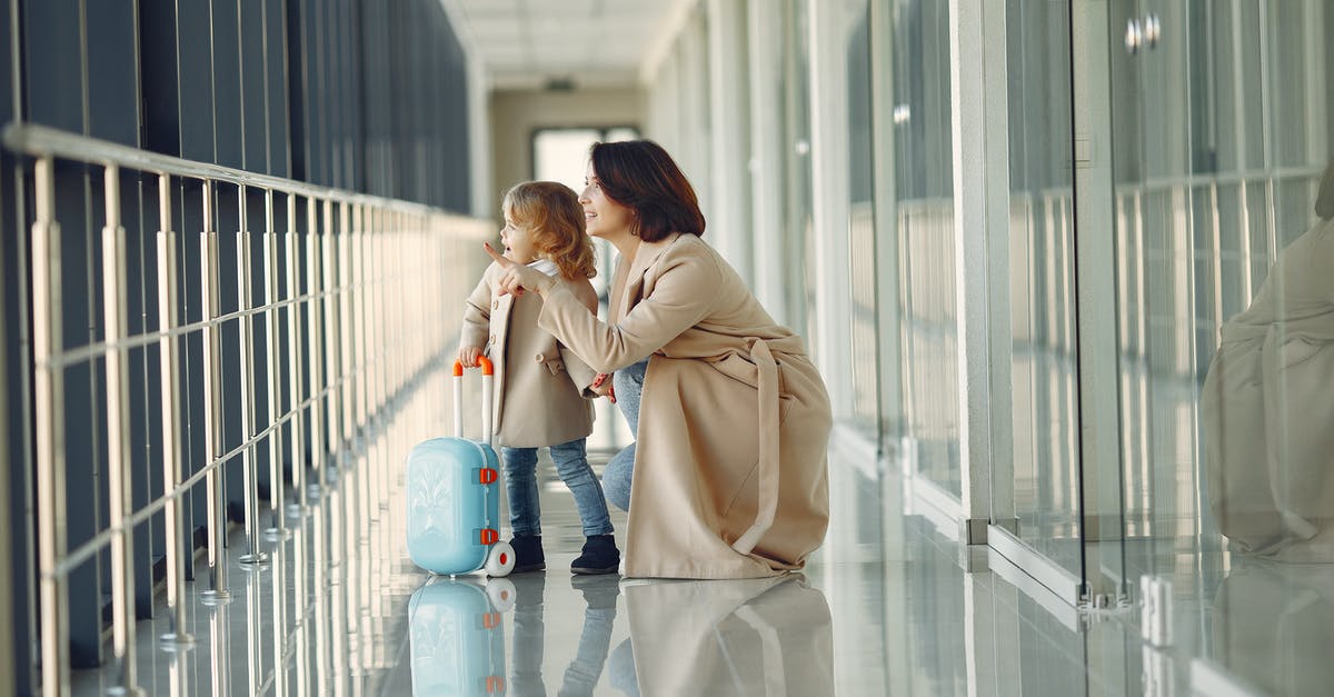 Extra baggage fees - Per flight or per ticket? - Side view full body of astonished cute little girl with kids suitcase and smiling mother pointing out window while walking together in contemporary airport hallway