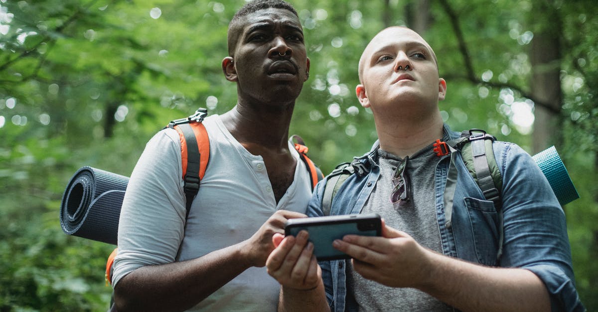 Fastest way of traveling between Berlin and Warsaw without using planes - From below of diverse lost travelers with backpacks exploring woodland and searching way in cellphone