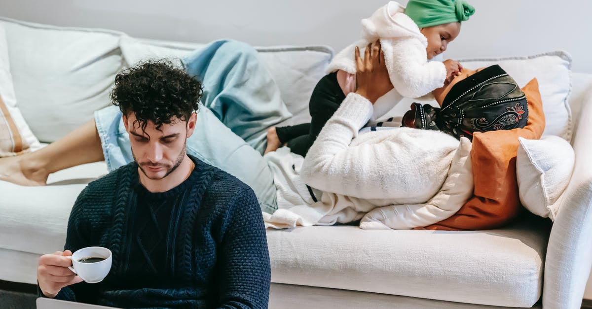 Father travelling with child from UK to Canada without Mother - High angle of loving African American mom caressing girl while dad drinking coffee and watching netbook at home