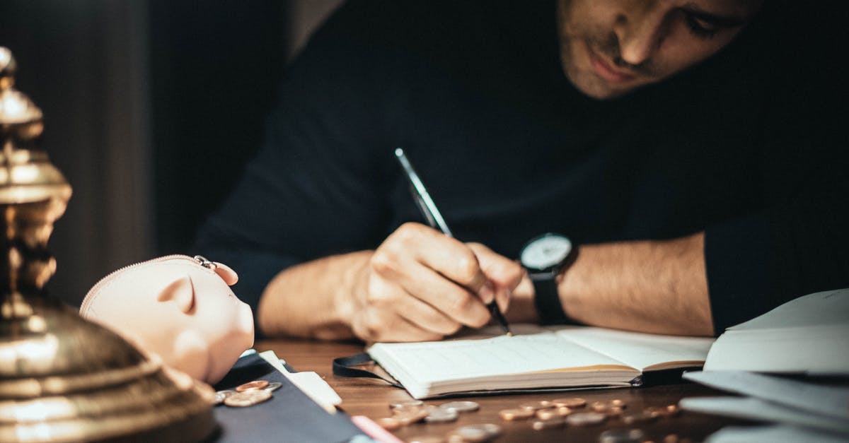 Fee for taking cash out of the EU - Crop elegant man taking notes in journal while working at desk with coins and piggybank in lamplight