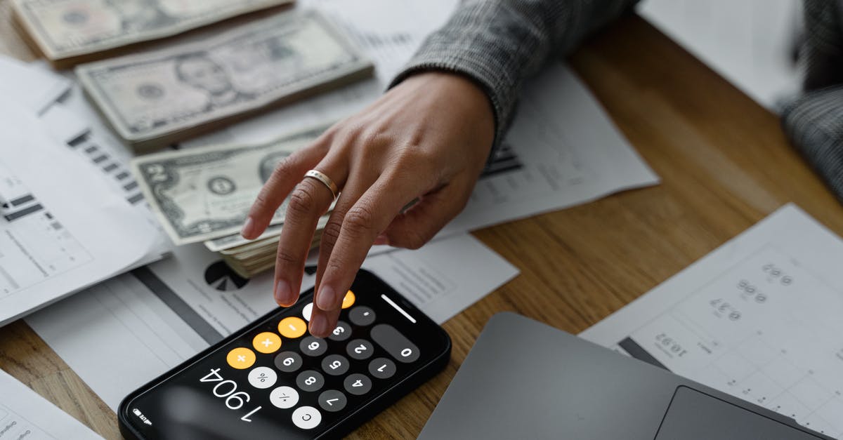 Fee for taking cash out of the EU - Hand of a Person Using a Calculator Near Cash Money on Wooden Table