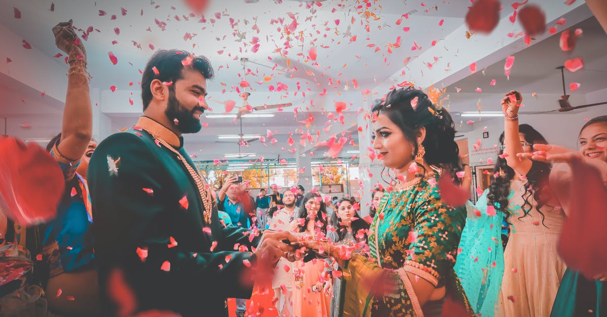 Filipino national getting a visa via a British partner - Indian people in bright festive clothes smiling and congratulating newlywed ethnic couple in falling red petals