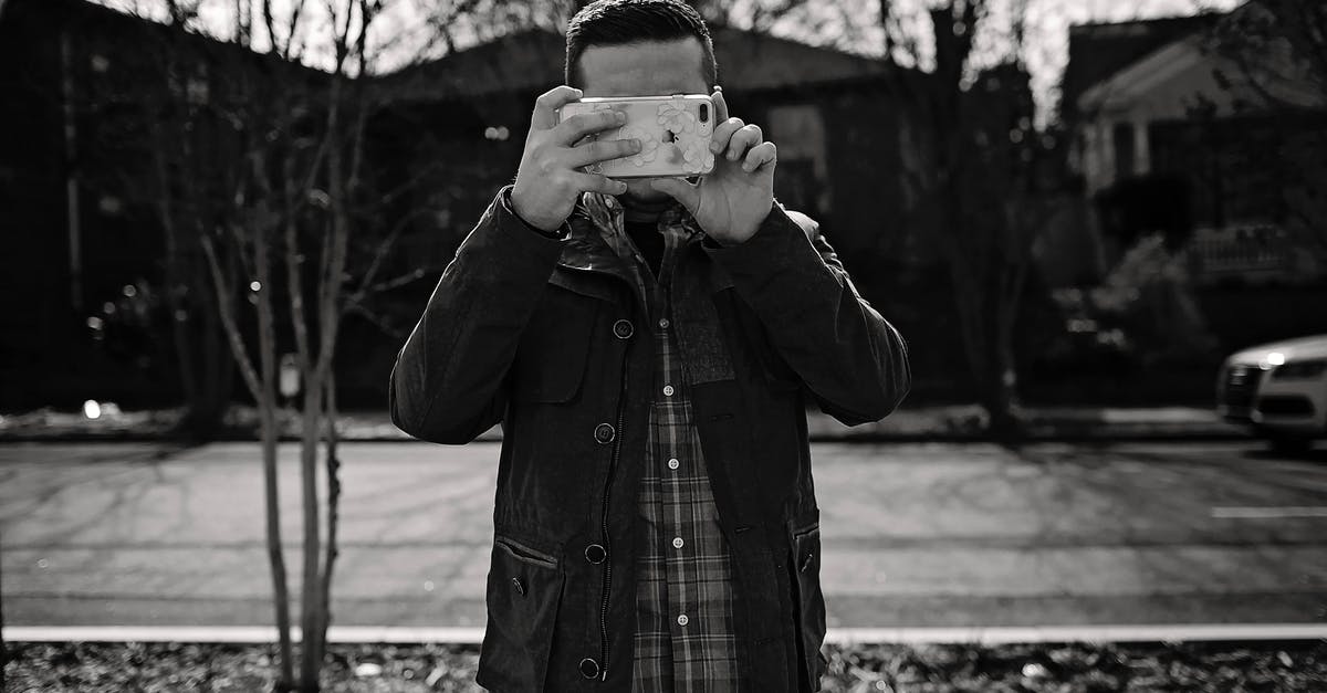 Filming via iPhone in clubs in Atlanta [closed] - Black and white shot of faceless man in casual clothes standing on pavement and taking photo on smartphone