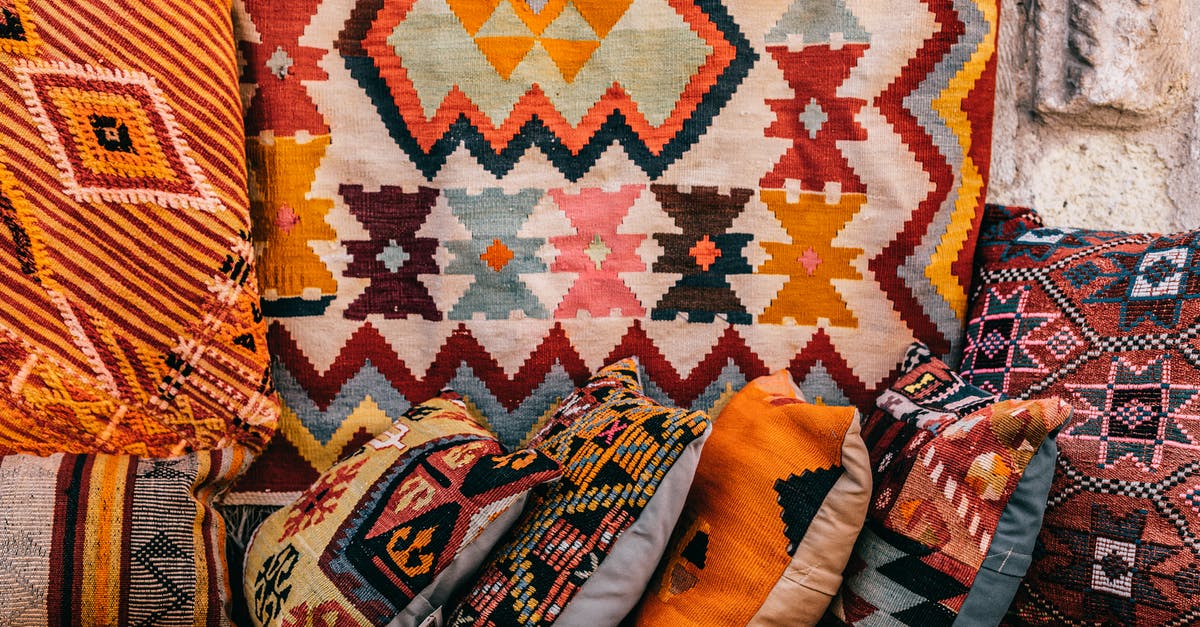 Finding Flights to One of Many Cities - Colorful pillows with patterns placed on couch near abundance of ornamental oriental carpets on bazaar in old city on street