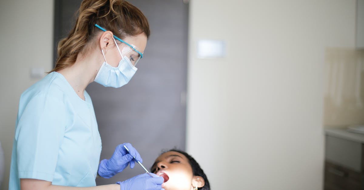 Finding job on Visit visa [closed] - Young female dentist in uniform mask gloves and eyeglasses with dental equipment treating teeth of black patient with closed eyes and opened mouth