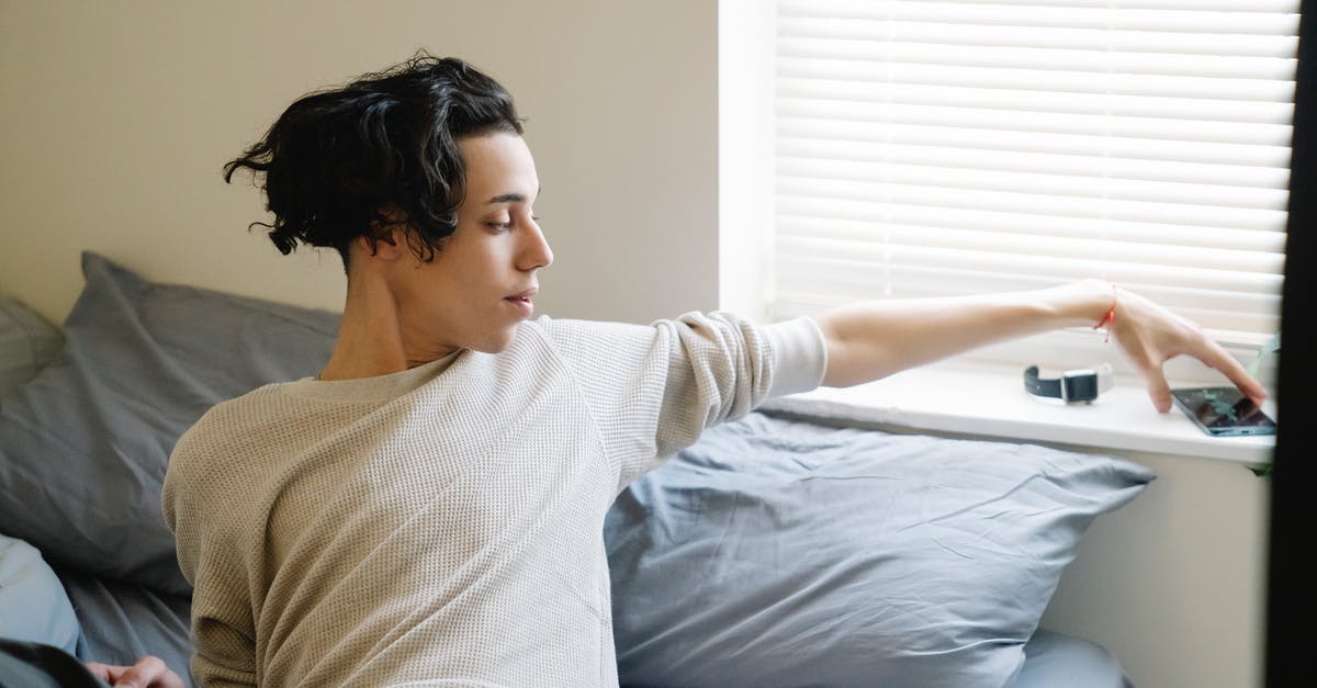 First time online airplane ticket? - Young ethnic male adolescent taking mobile phone from windowsill after awakening in morning in bedroom