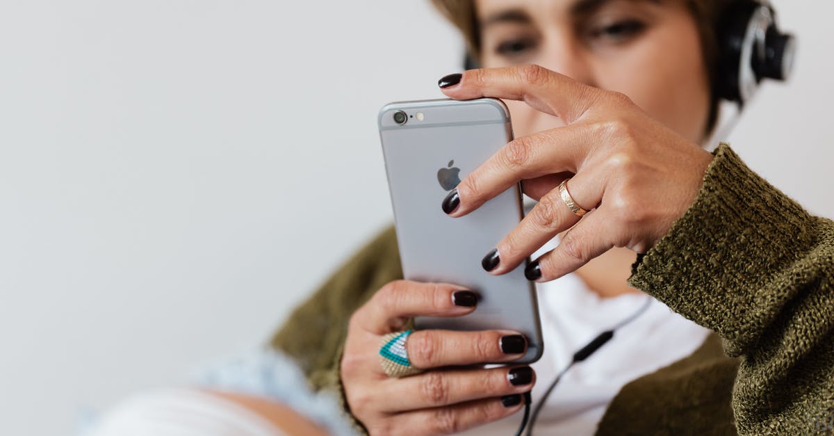 First time Schengen Visa application for france - Crop blurred focused female in casual warm clothes with classy ring surfing contemporary cellphone while enjoying favorite music via wired headphones against white plain wall