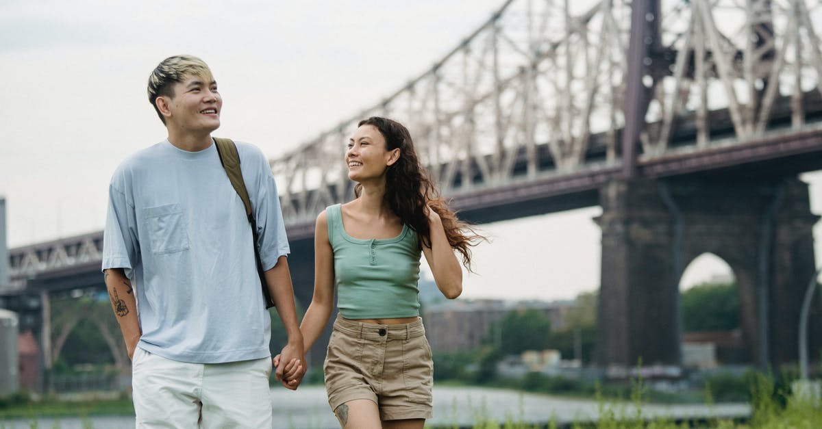 First time traveler to the US via connecting flights - Happy ethnic couple holding hands while strolling in park near bridge