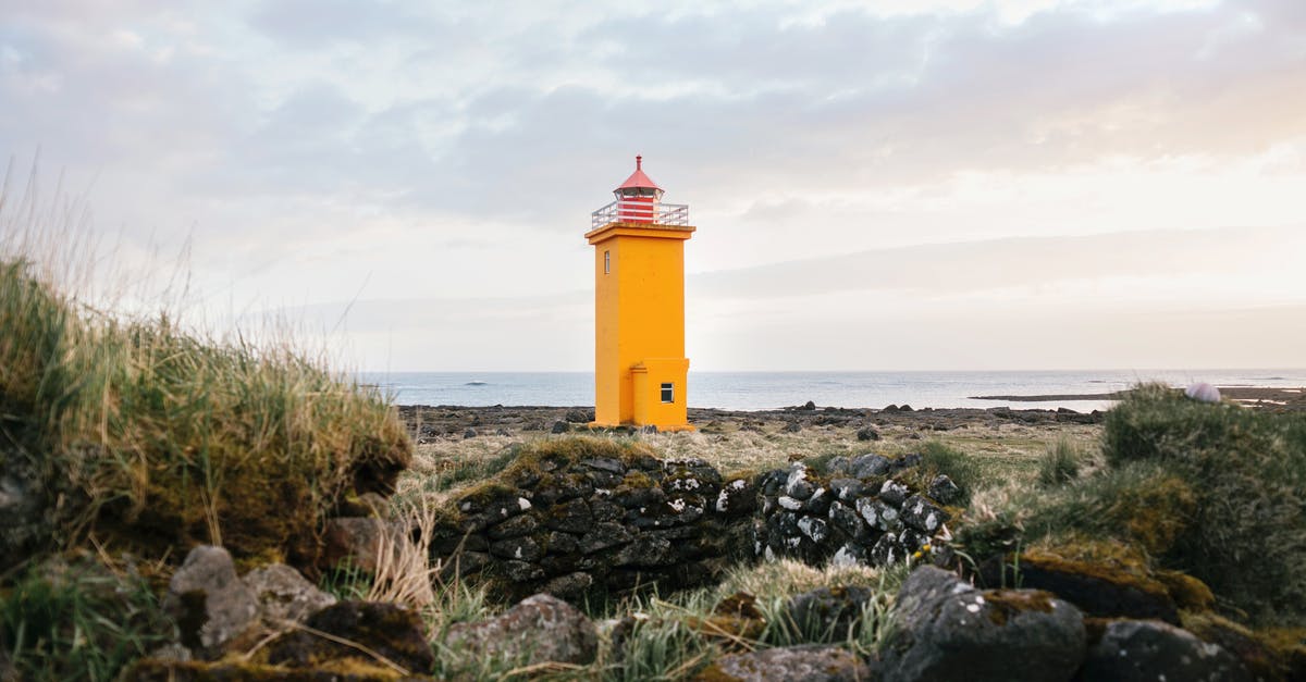 Flashing yellow beacon in Canada - Picturesque view of seashore covered with stones and grass and bright yellow lighthouse against cloudy sky at daytime