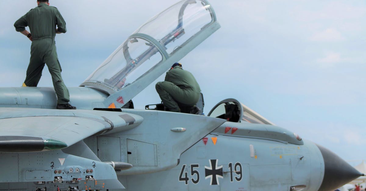 Flight cancelled due to strikes - Low angle of unrecognizable male pilots in uniforms standing on aged gray multirole combat aircraft before flight against cloudy sunset sky